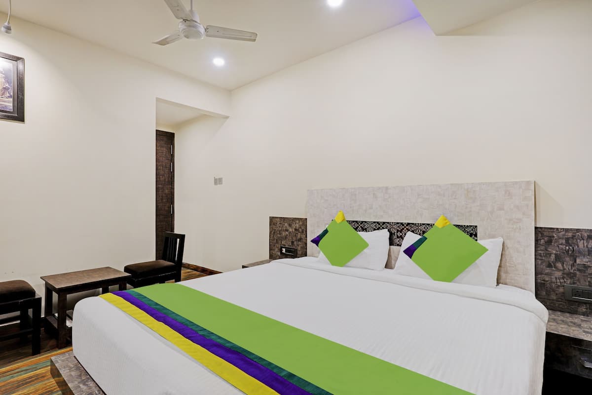 A hotel room with a large bed, a desk, a chair, a ceiling fan, and a framed picture on the wall.