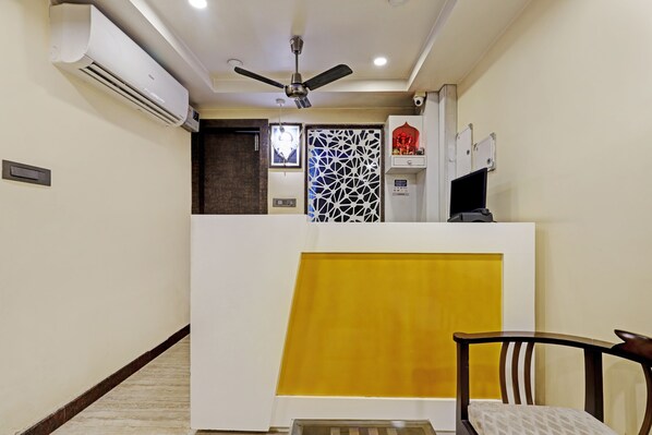 Zona de recepción con ventilador de techo, aire acondicionado y mostrador con panel amarillo.
