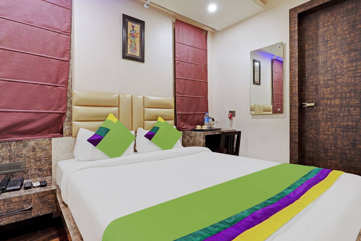 A hotel room with a bed, a nightstand, a mirror, a door, and a window with a curtain.