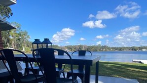 An outdoor patio with a table and chairs, a concrete floor, and a view of a lake with trees and buildings in the background.