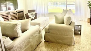 A living room with a large flat-screen TV, a sofa, a chair, and a coffee table.