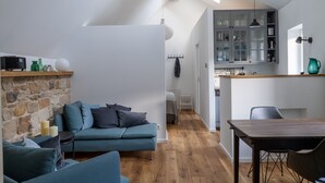 Un salon moderne avec un canapé bleu, une table à manger et un coin cuisine doté de placards et d’un luminaire suspendu.
