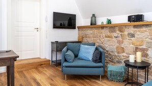 Un salon chaleureux avec une cheminée en pierre, un canapé bleu, une table basse en bois et un téléviseur à écran plat fixé au mur.