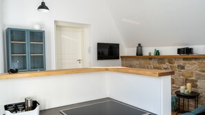 Une cuisine moderne dotée d’une cuisinière intégrée, d’un plan de travail en bois, d’un mur en pierre et d’un téléviseur fixé au-dessus d’une étagère.