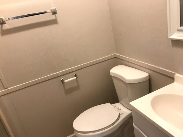 Un baño pequeño con inodoro, un rollo de papel higiénico y lavamanos.