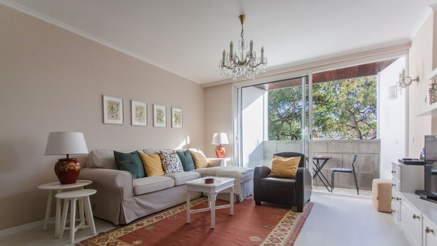 Een zithoek met een bank, salontafel en stoelen, een kroonluchter, ingelijste foto's aan de muur en een uitzicht door een glazen deur.