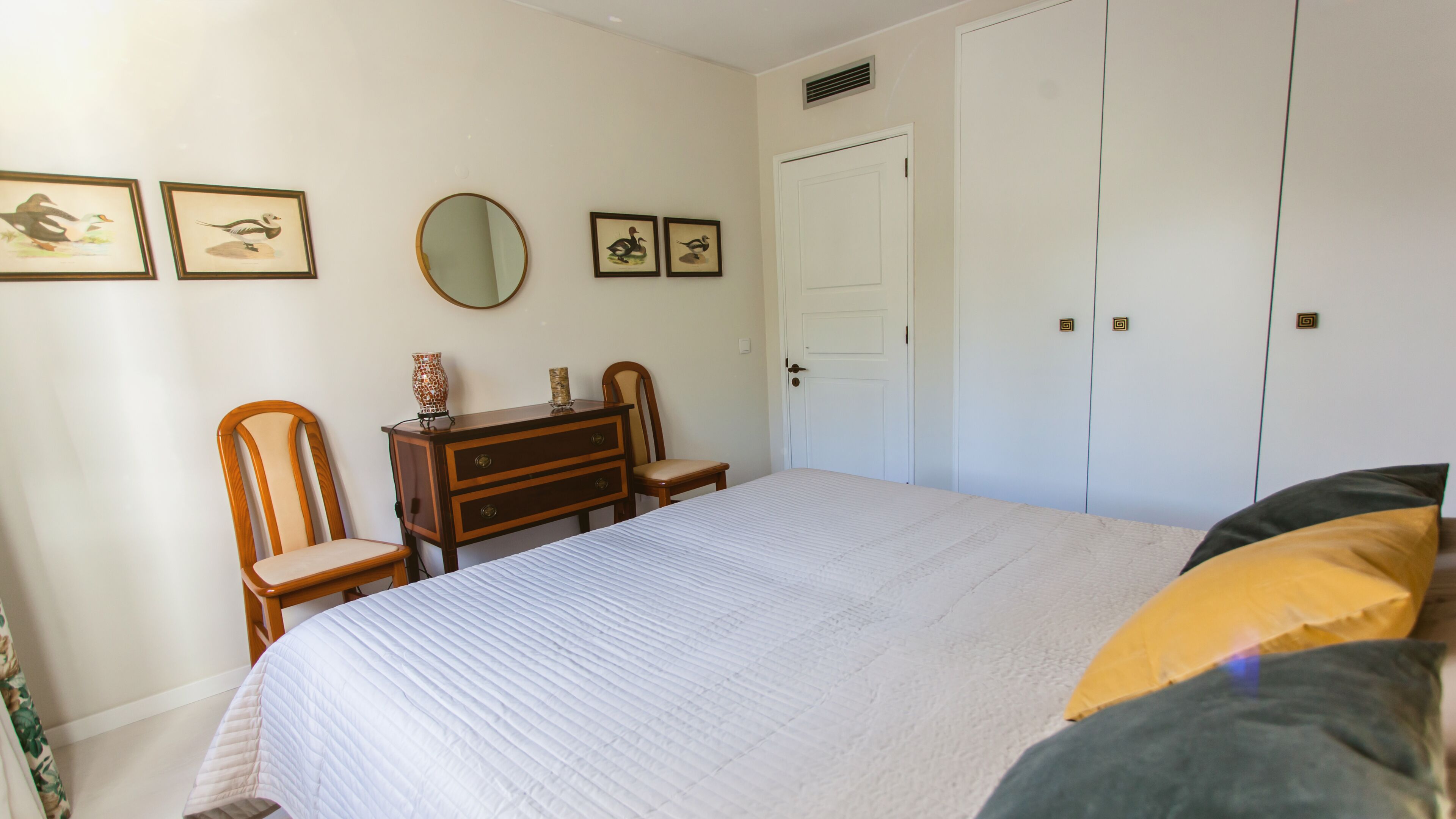 Een slaapkamer met een bed, een kaptafel, een stoel, een spiegel en een kledingkast.