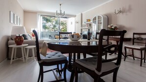 Een eethoek met een ronde tafel, stoelen, een vaas en een boekenkast.