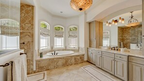 Ein luxuriöses Badezimmer mit einer großzügigen Freisitzbadewanne, einem Doppelwaschbecken mit großem Spiegel und drei Bogenfenstern mit gemusterten Vorhängen.