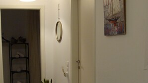 Ein Wohnzimmer mit grauem Sofa, einem Blumentopf, einem Wandspiegel und einem Gemälde eines Segelboots.