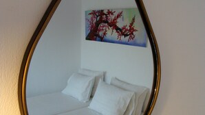 Ein Bett mit weißer Bettwäsche und Kissen, ein Baum mit roten Blättern als Wandbild und ein Spiegel mit goldener Rahmung.