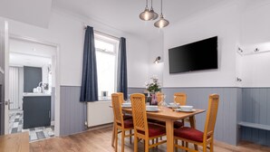 Un coin repas avec une table et des chaises en bois, un téléviseur à écran plat fixé au mur et une fenêtre avec des rideaux.