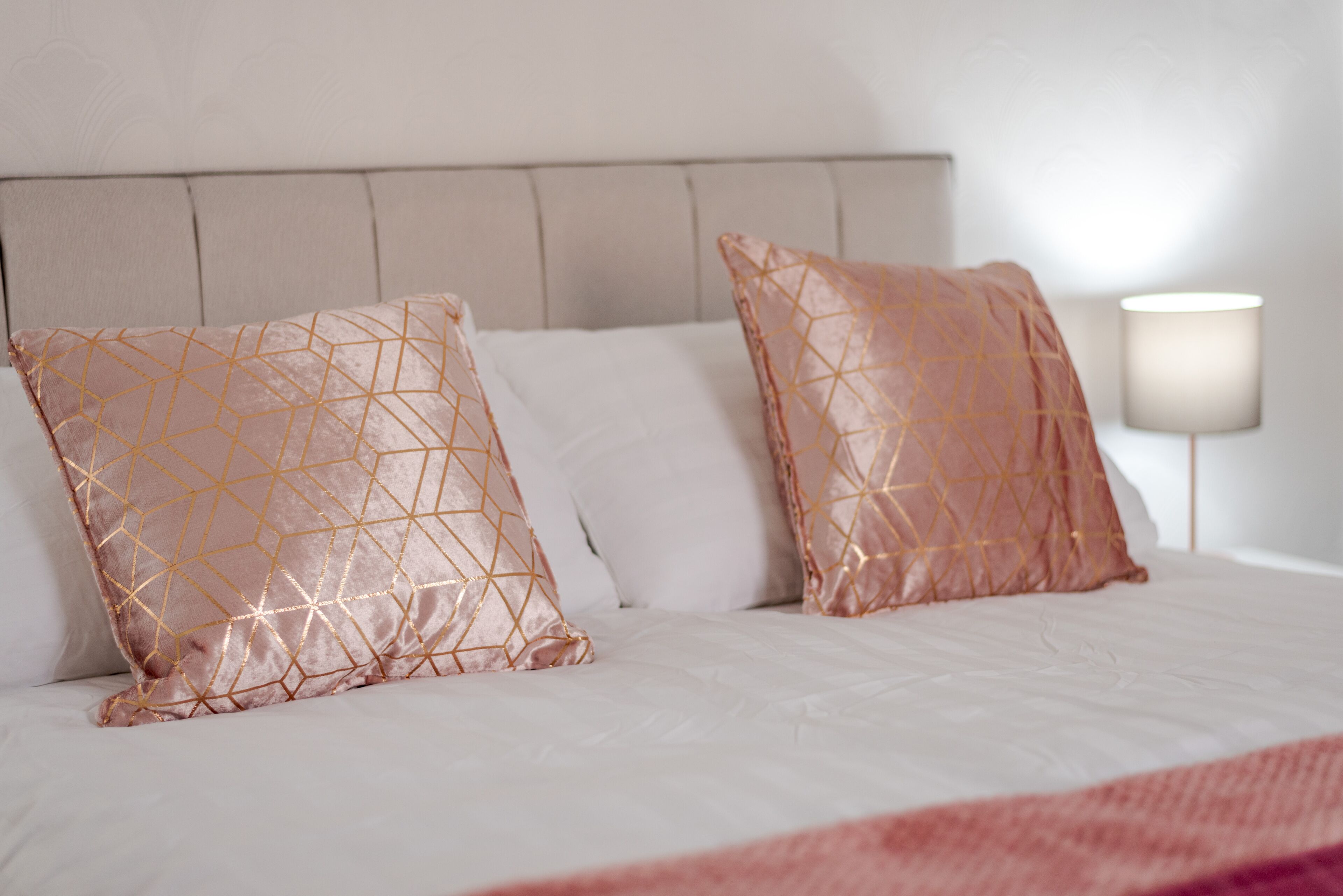 A bed with a headboard, two decorative pillows, and a bedside lamp.