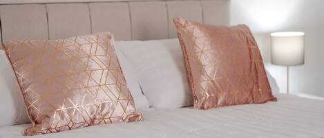 A bed with a headboard, two decorative pillows, and a bedside lamp.