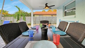 Un patio techado con mobiliario de mimbre, una mesa con vasos de plástico de colores y un ventilador de techo.