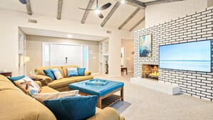 Una sala de estar con televisor grande, chimenea y vista al mar.