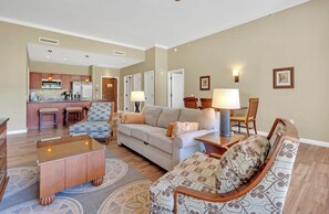A living room with a sofa, armchairs, a coffee table, and a dining area with a kitchen in the background.