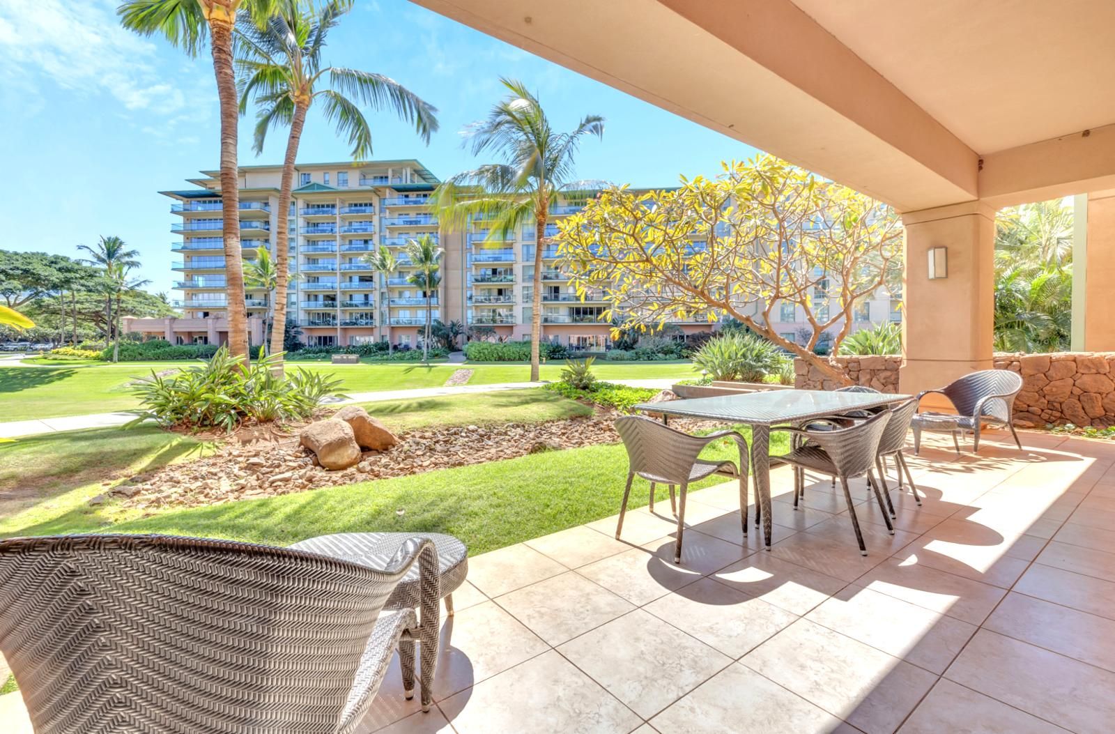 A covered outdoor area with a table and chairs, a stone wall, and a view of a multi-story building with balconies.