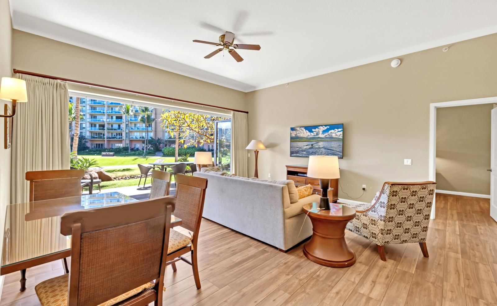 A hotel room with a dining area, a sofa, a TV, and a view of the outside.