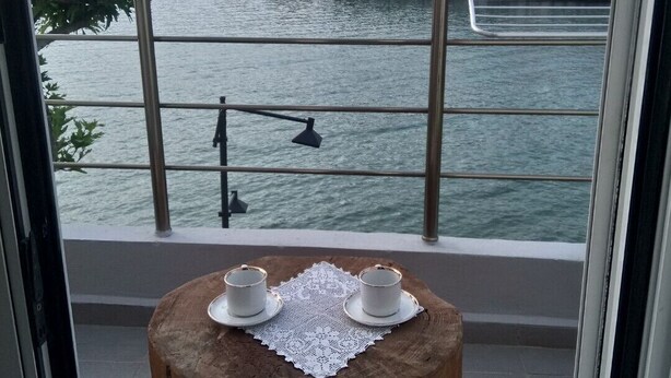A balcony with a wooden stool, two white cups, and a lace doily. A railing with a red object on top is visible. - Ilio Socrates Triple room with sea view. (Thassos)