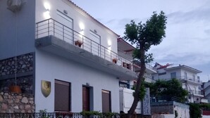 A modern two-story building with a balcony, potted plants, and a stone wall. - Ilio Socrates Triple room with sea view. (Thassos)