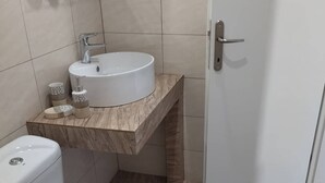 A bathroom with a toilet, sink, and door. - Ilio Socrates Triple room with sea view. (Thassos)