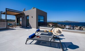 Un espace extérieur moderne, aménagé avec une table, des chaises et un chapeau de soleil, situé sur une terrasse offrant une vue sur la côte.