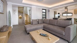 Uma sala de estar moderna com um sofá seccional cinza, uma mesa de centro de madeira e uma escada que leva a um andar superior.