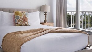 Ein Hotelzimmer mit einem Bett, einem Deckenventilator, einem Nachttisch mit Lampe und einem großen Fenster mit Blick ins Freie.