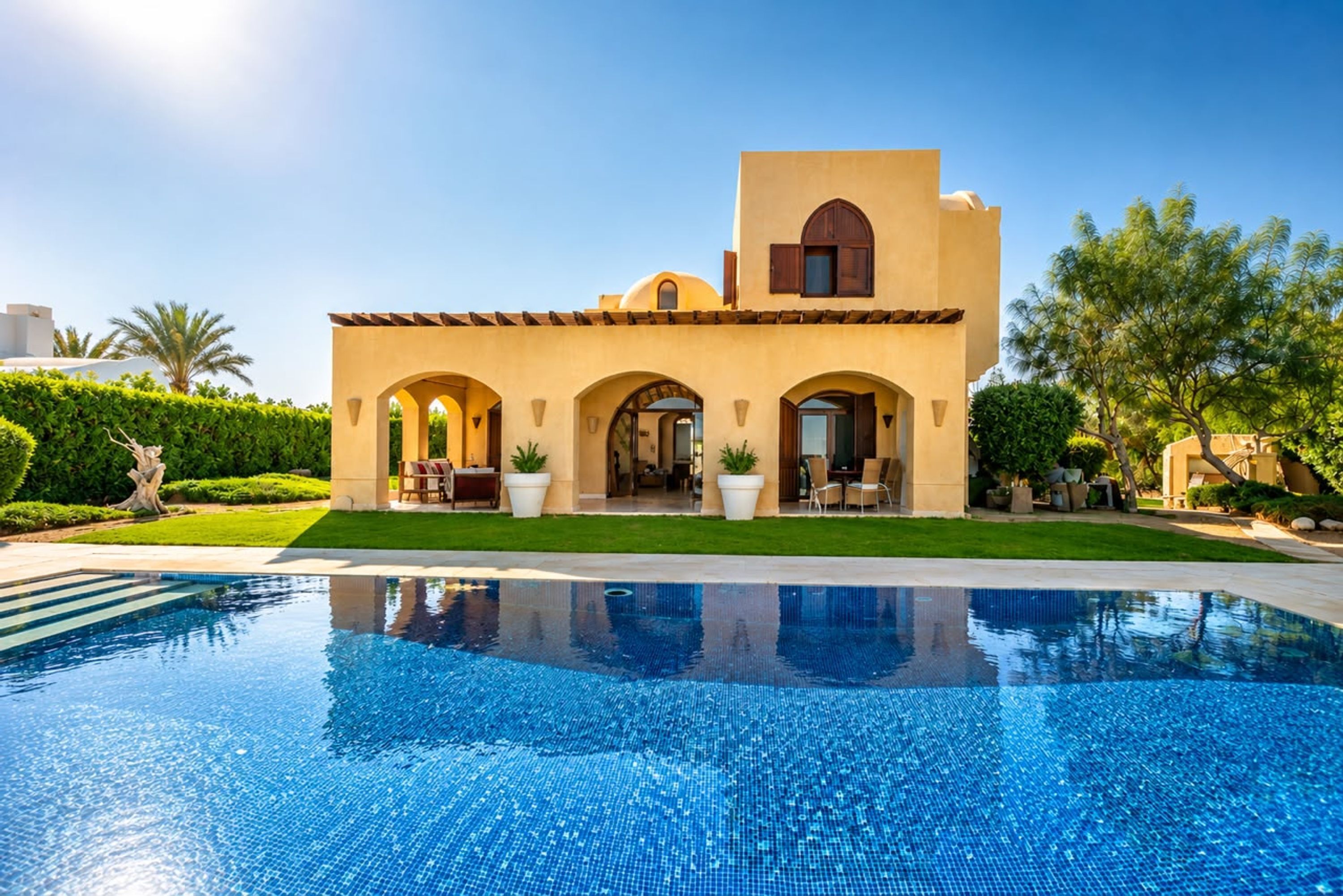 Una villa de estilo mediterráneo con piscina, arcos y techo plano.