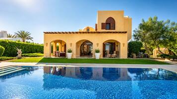 Una villa de estilo mediterráneo con piscina, arcos y techo plano.