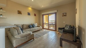 A living room with a sofa, a coffee table, a TV, and a sliding glass door leading to a balcony. - Vesta - Luxury APT - 1BR - Sabina (El Gouna)