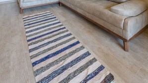 A living room with a beige sofa, a striped rug, and a kitchen in the background. - Vesta - Luxury APT - 1BR - Sabina (El Gouna)