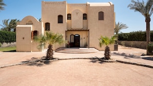 A traditional building with a central entrance, palm trees, and a stone wall in the background. - Vesta - Luxury Villa - 4BR - North Golf (El Gouna)
