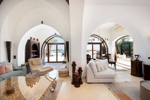 A spacious living room with high ceilings and arched windows, featuring a beige sofa, a white sofa, and a glass coffee table. - Vesta - Luxury Villa - 4BR - North Golf (El Gouna)