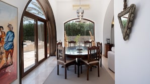 A dining area with a glass table and chairs, a painting on the wall, and a view of the outdoors. - Vesta - Luxury Villa - 4BR - North Golf (El Gouna)