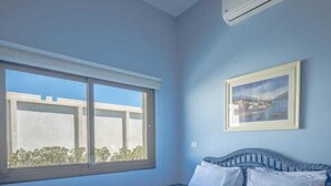 A bedroom with a large bed, a window, and an air conditioning unit.