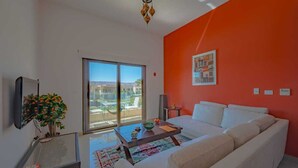 A living room with a white sofa, a coffee table, a TV, and a large window with a view of buildings.