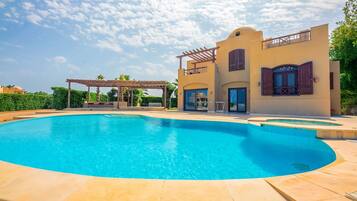 A swimming pool with a curved design, a pergola, and a building with a balcony and large windows.