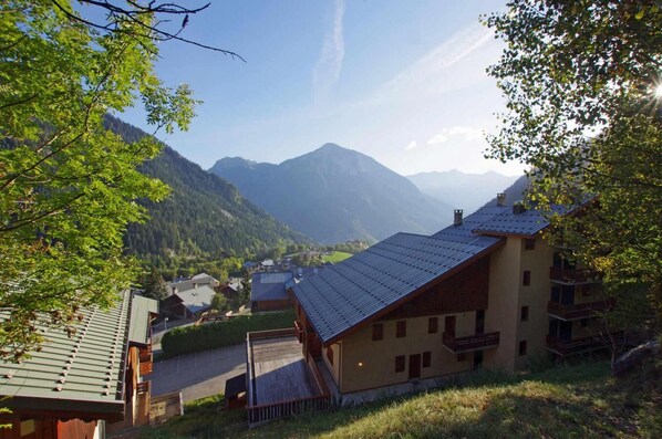 Un village de montagne avec des maisons traditionnelles en bois, une route pavée et une vue sur les montagnes lointaines.