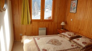 Un dormitorio con decoración de madera, una cama con colcha estampada, una mesita de noche con lámpara y una ventana con vistas a un paisaje nevado.