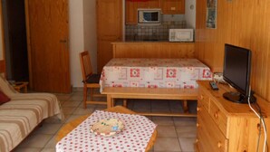 Habitación pequeña con una cama, una mesita con mantel, televisor, microondas y armarios de madera.