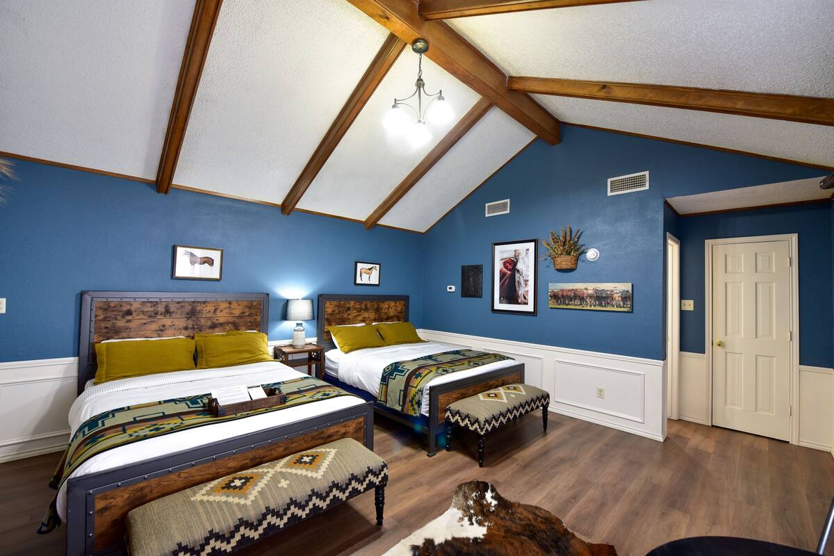 A bedroom with two beds, a wooden ceiling, and a blue wall.