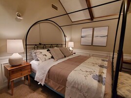 Quarto com cama de dossel, duas mesas de cabeceira, um criado-mudo e um ventilador fixado na parede.