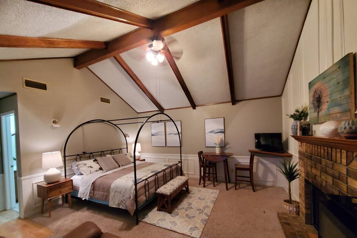 A bedroom with a four-poster bed, a fireplace, a television, and a small table with chairs.