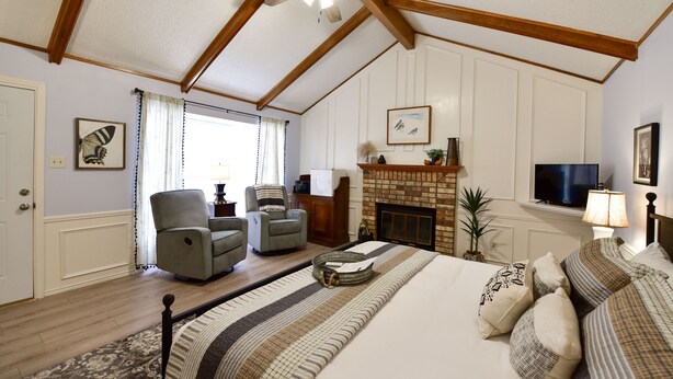A bedroom with a large bed, two armchairs, a fireplace, and a ceiling fan. - Butterfield Inn Main Street Cottages (Fort Davis)