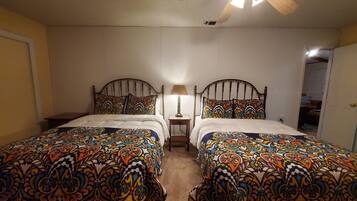A double room with two beds, each with a patterned bedspread, a ceiling fan, and a nightstand with a lamp.