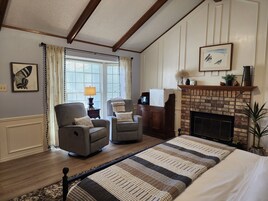 Una sala de estar acogedora con chimenea, dos sillones, una cama grande y una ventana con cortinas.