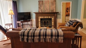 A living room with a fireplace, a television, and a ceiling fan. - Butterfield Inn Main Street Cottages (Fort Davis)