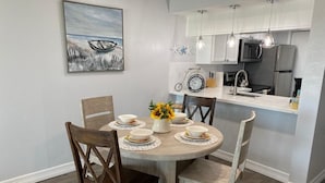 A dining area with a round wooden table, four chairs, and a vase with yellow flowers. A painting of a boat on water is on the wall. - Oceanview Beach Getaway, Great balcony!! (Galveston)